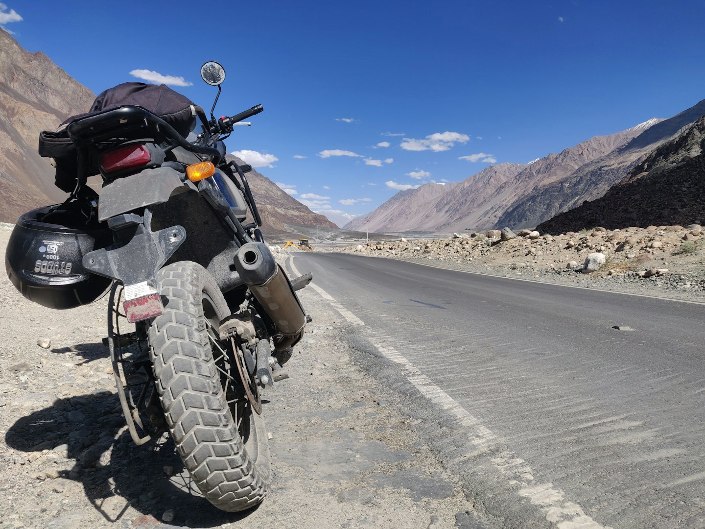 Adventure motorcycle parked on gravel shoulder near mountains.