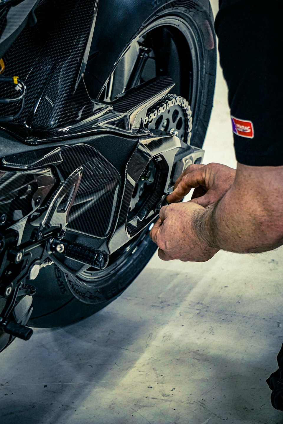 A mechanic adjusts the chain and sprocket on a motorcycle.