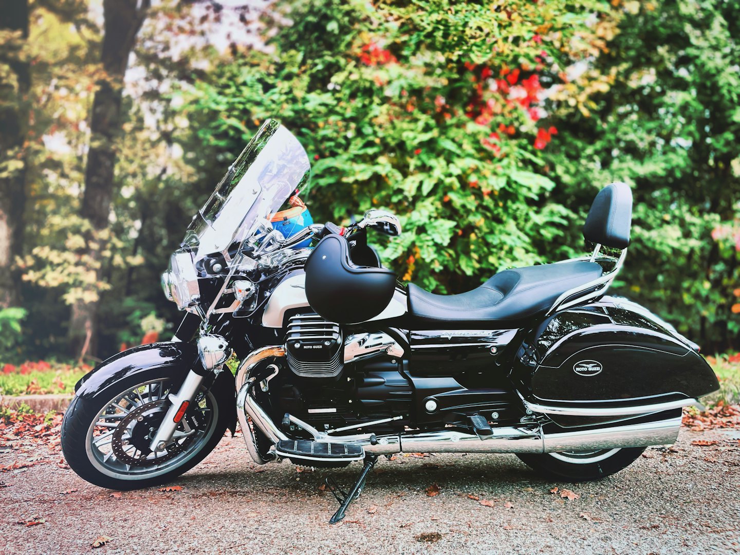 Black and chrome touring motorcycle parked on asphalt with leaves.