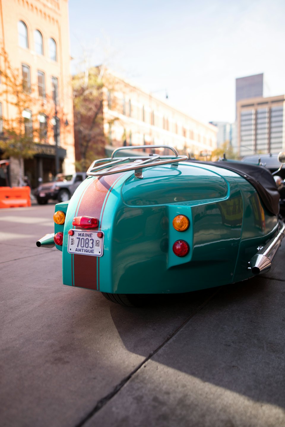 Teal vintage sidecar with racing stripes parked on city street.