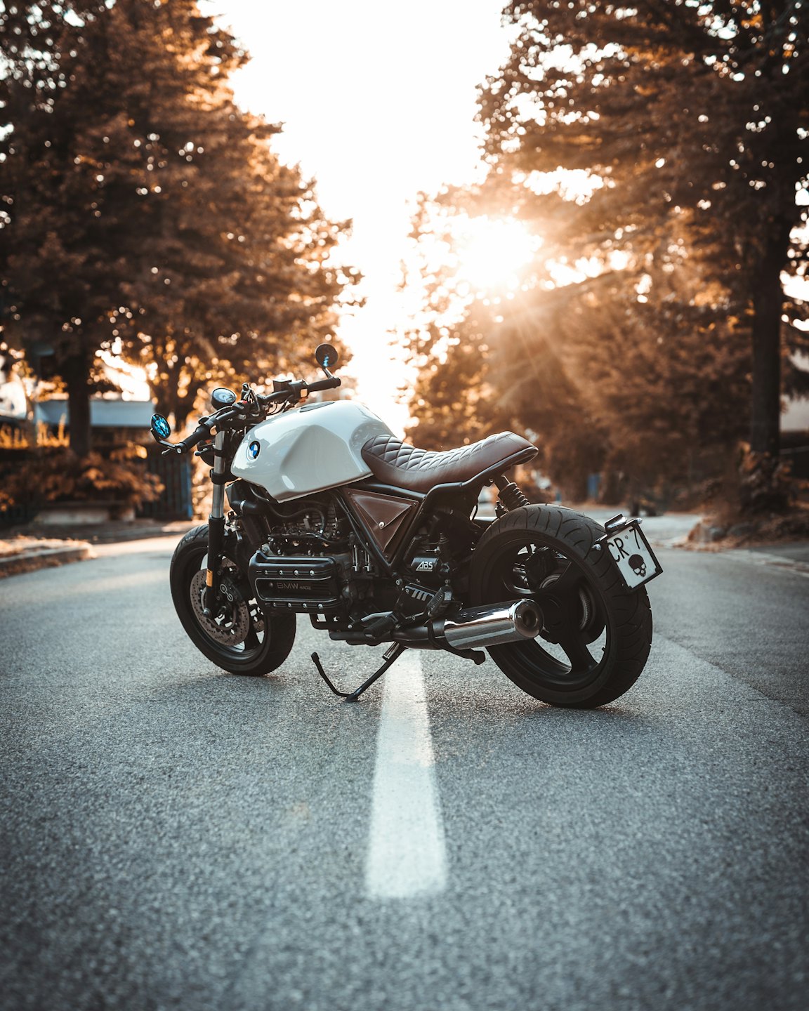 A cream and brown vintage motorcycle parked on a road at sunset.
